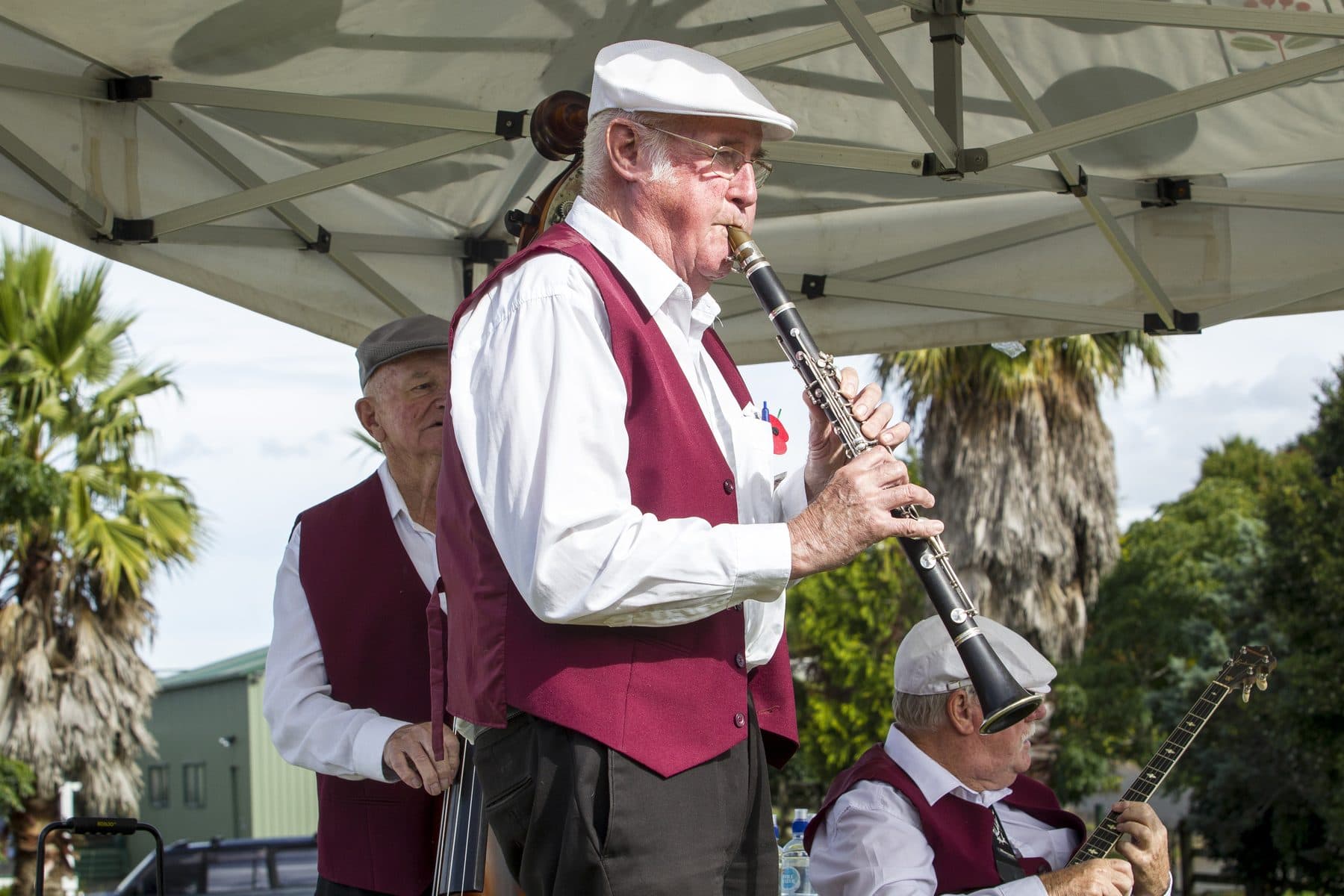 A man in a red waistcoat playing the clarinet with a band under a gazebo.