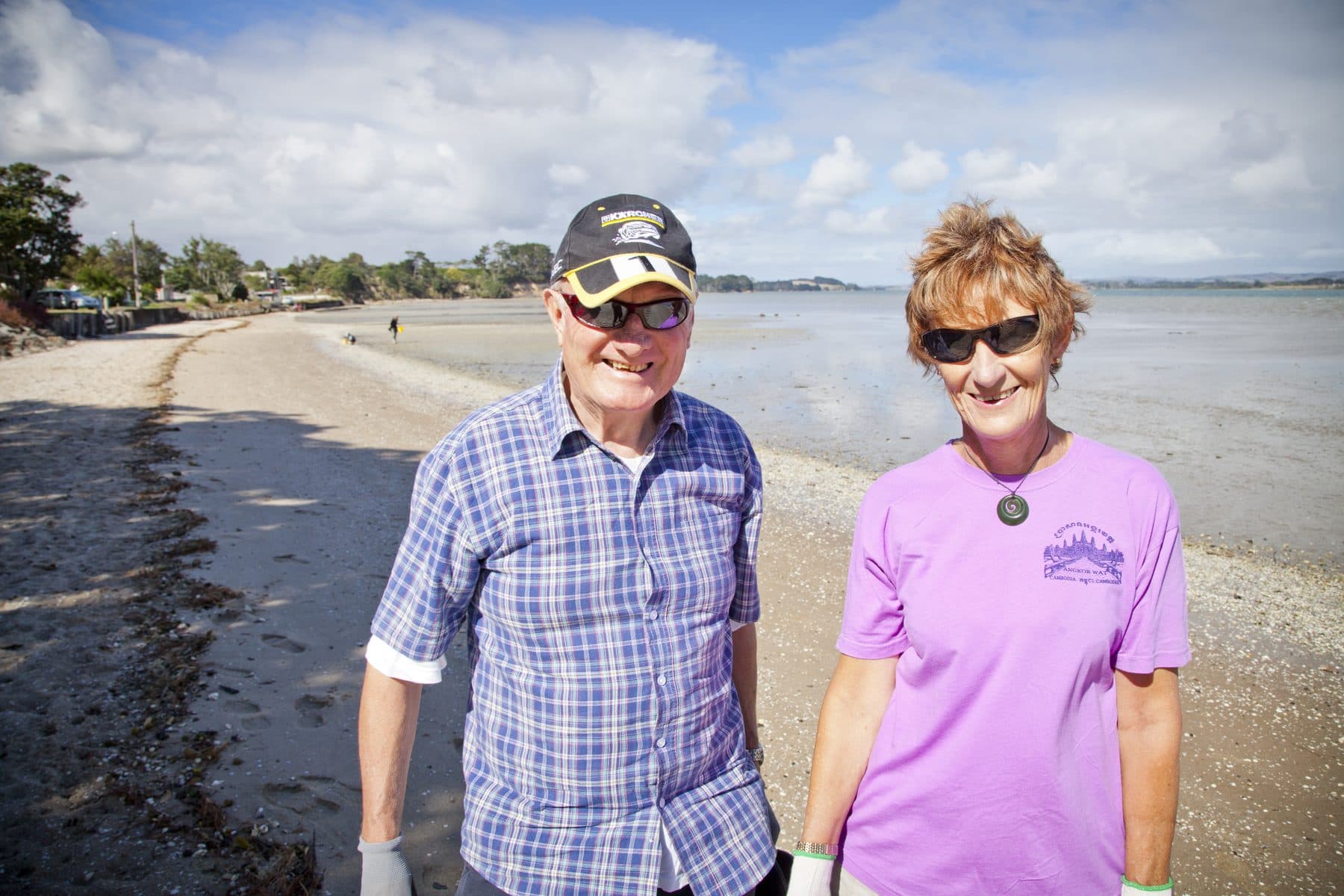 A couple standing on a beach at low tide, smiling, with hills across the water.