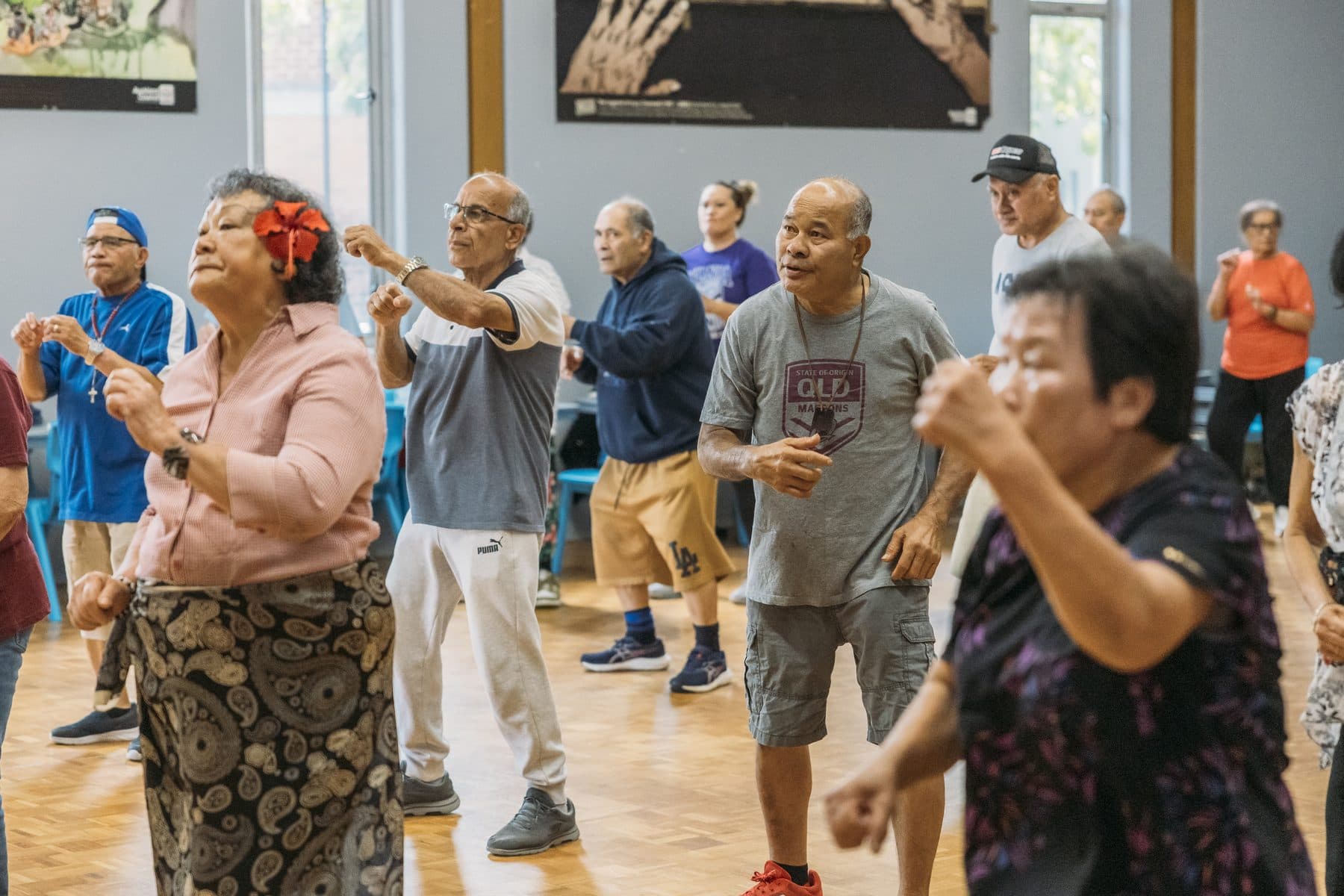 Older people doing an exercise class together in a community hall, arms raised and smiling.