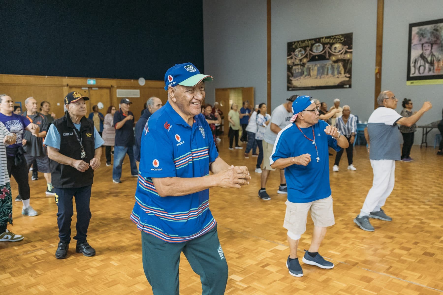 Men in bright shirts stepping and clapping in an exercise class in a hall.
