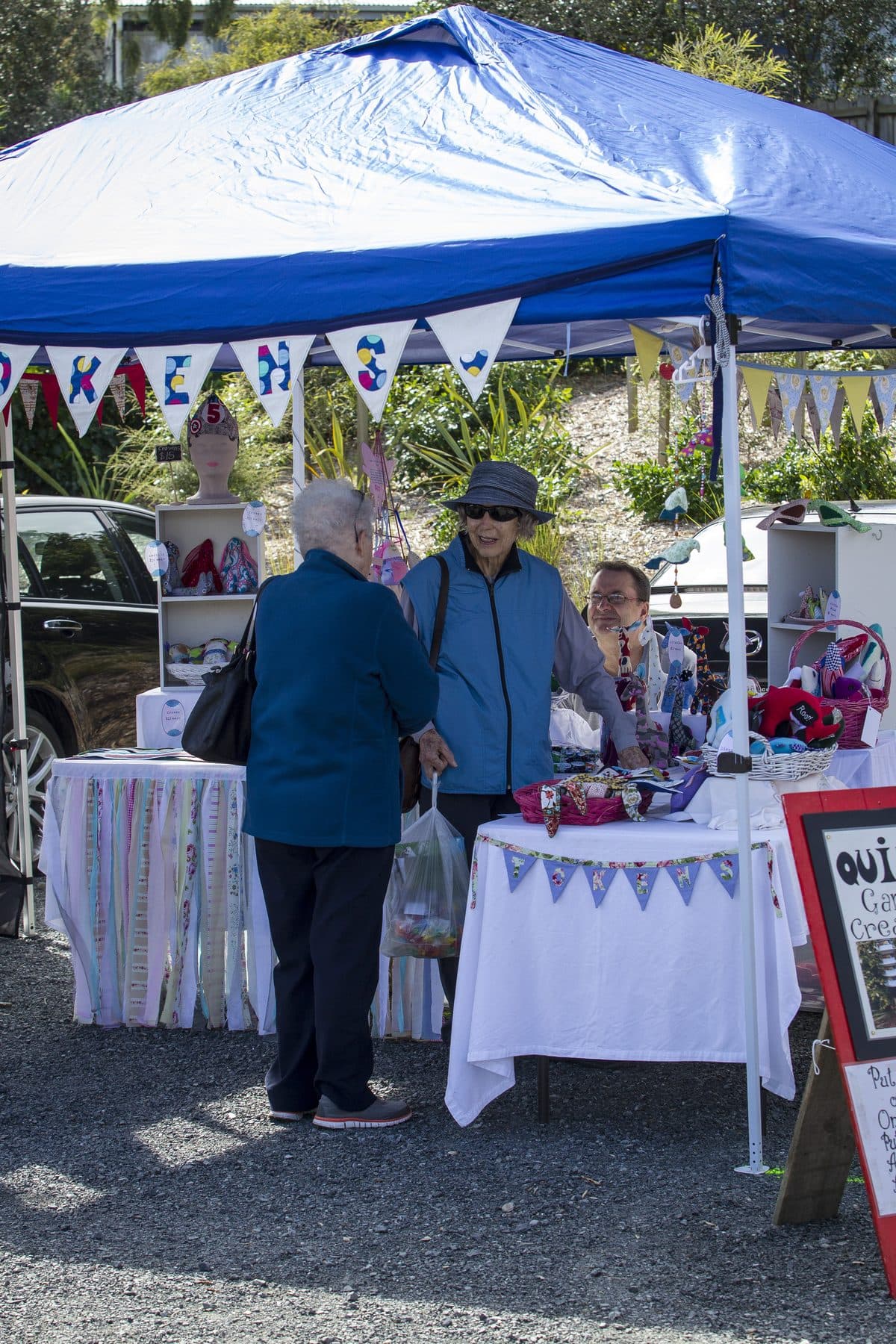 Two women in sun hats looking at a craft stall under a blue gazebo.