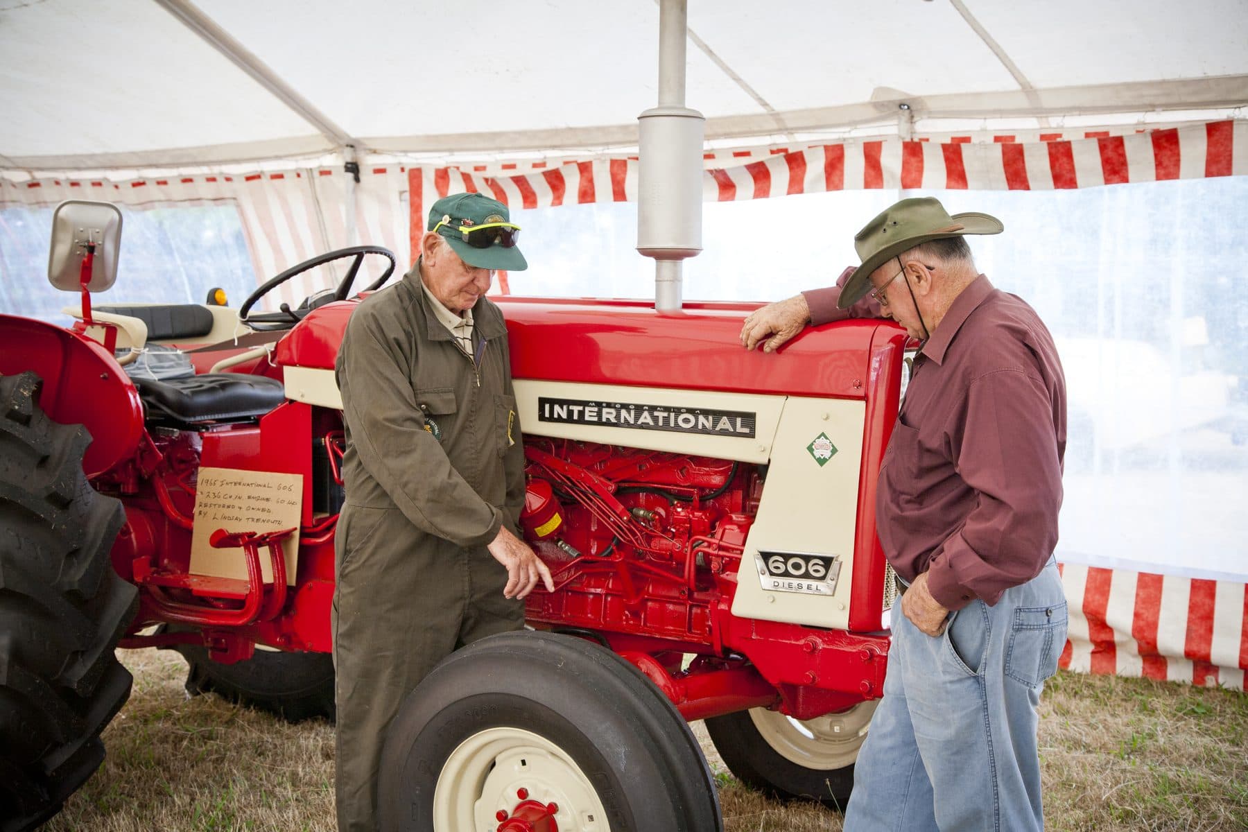 Two men admiring a red vintage tractor in a marquee at an A and P show.